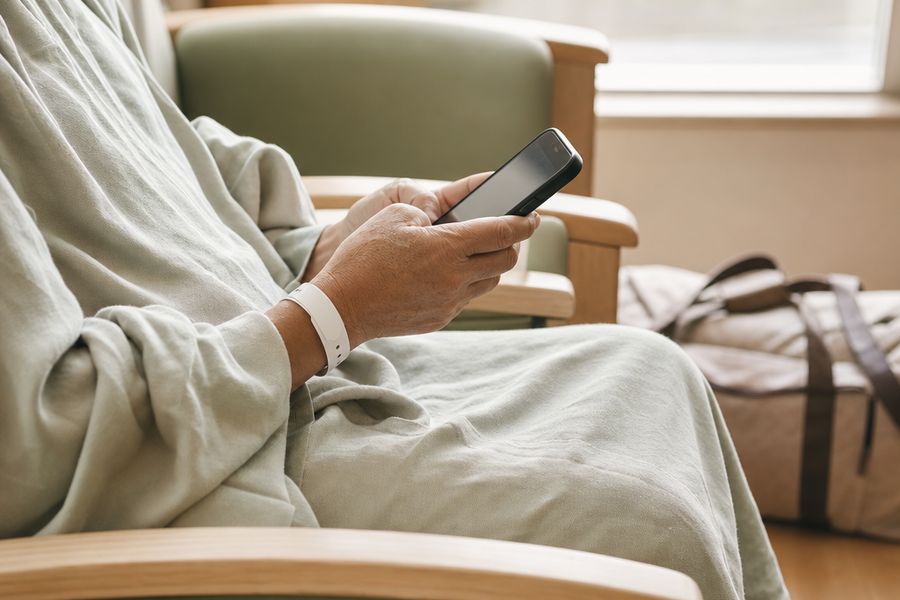 A patient’s hands holding a phone, a hospital wristband on one wrist